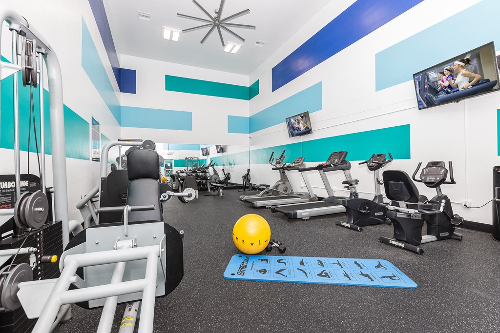 a gym with cardio machines and weights and a yellow ball on the floor