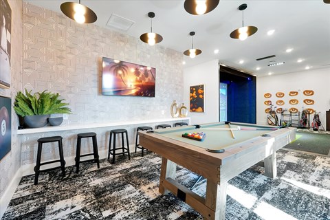 A pool table is in the middle of a room with a bar area.