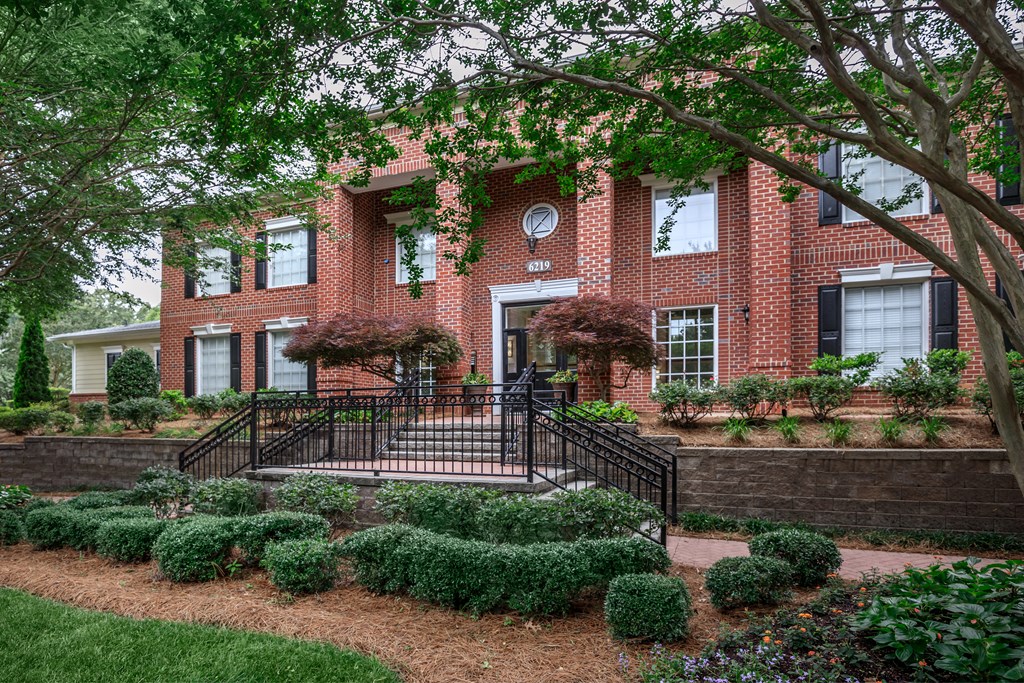 the front of a brick house with stairs and a garden