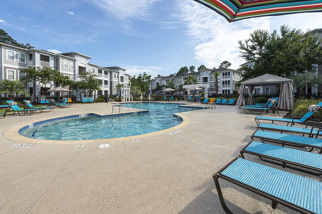 a resort style pool with blue lounge chairs and an apartment building in the background