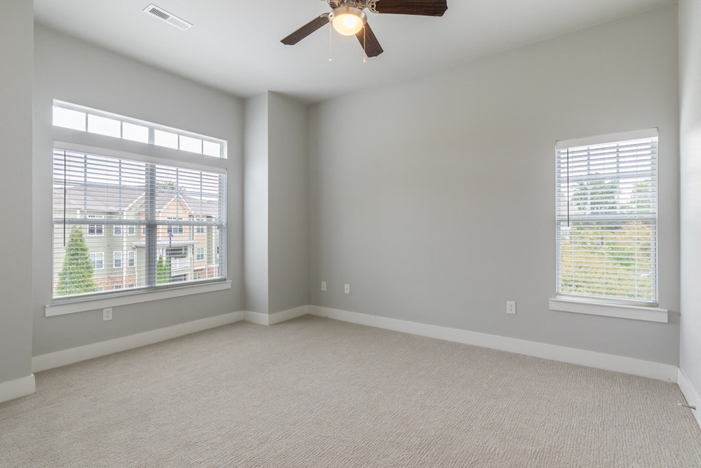 an empty living room with two windows and a ceiling fan