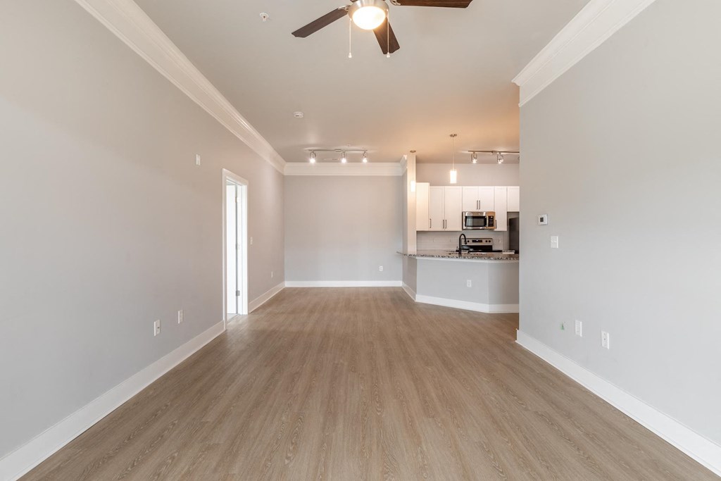 an empty living room with a ceiling fan and a kitchen