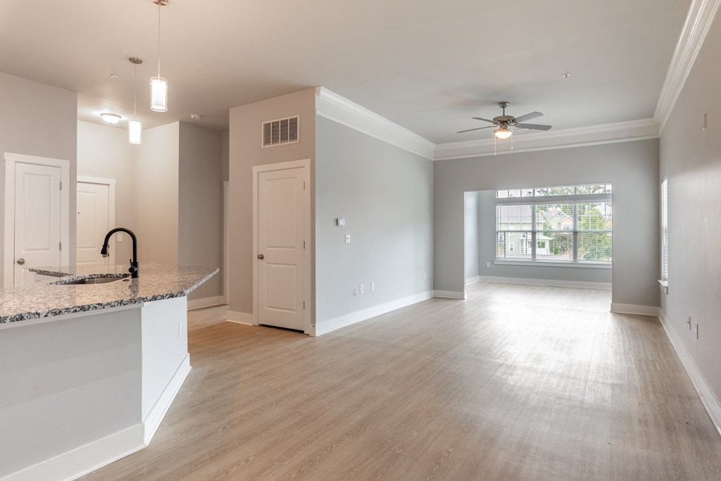 an empty living room with a kitchen and a ceiling fan
