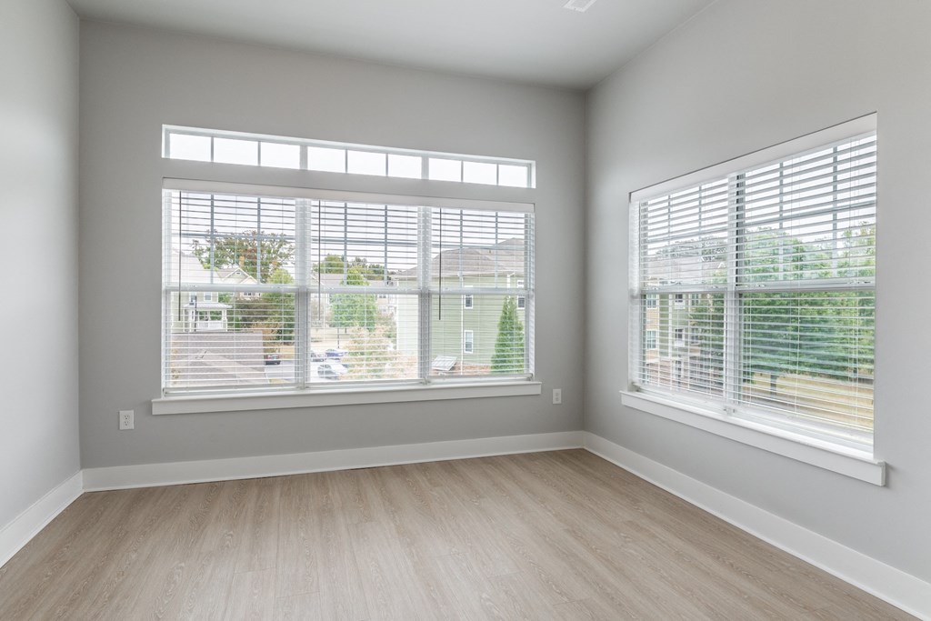 an empty room with two windows and wood floors