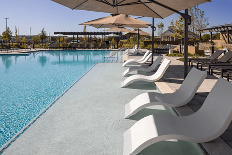 A pool with white chairs and a shade structure at Boardwalk at Research Park apartments in Huntsville, AL.