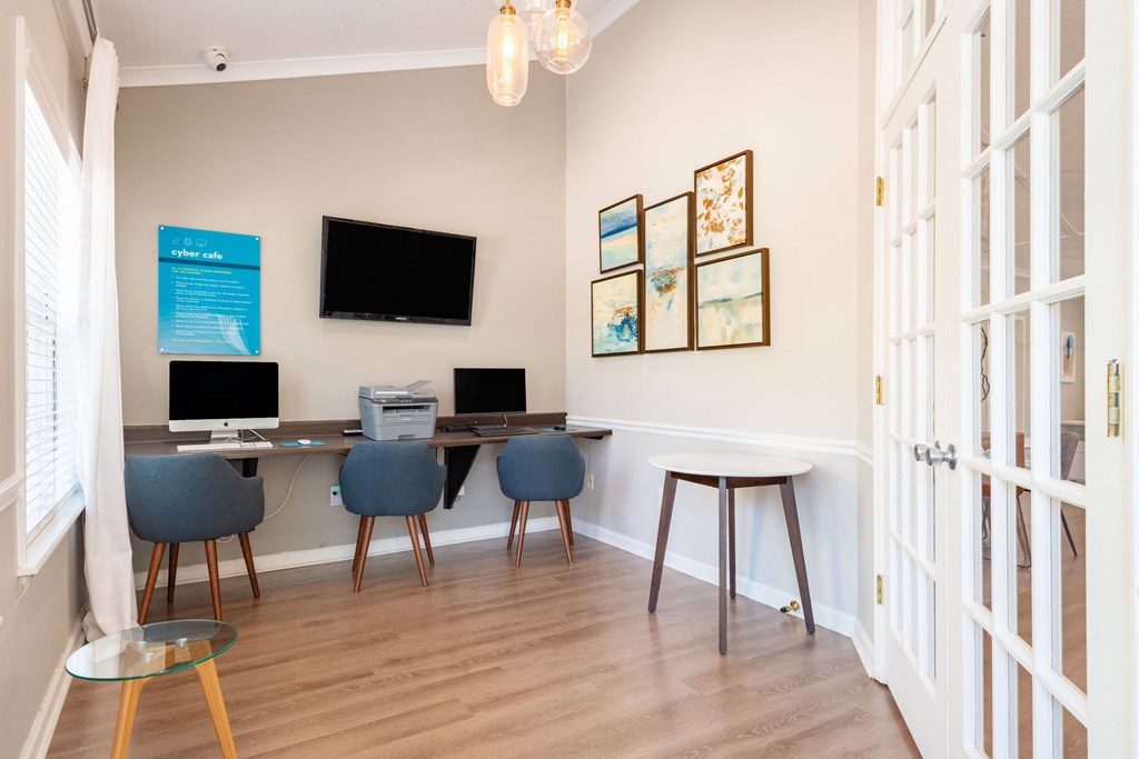 a room with a table with three computers on it and a tv on the wall