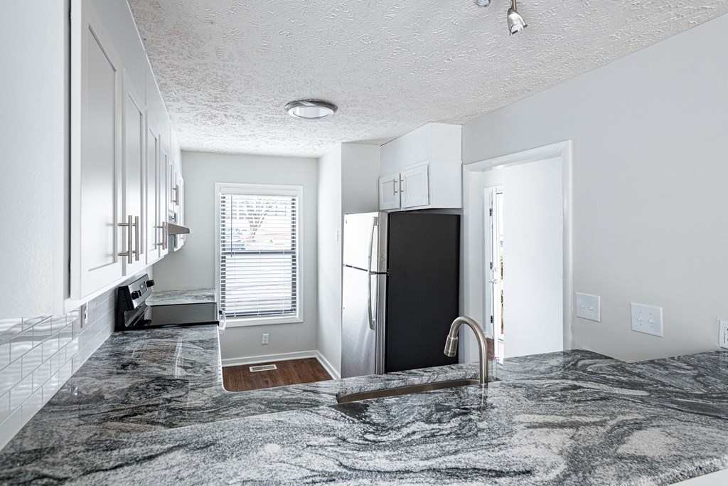 an empty kitchen with granite counter tops and a refrigerator