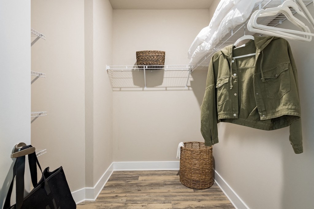 a walk in closet with a white jacket hanging on the wall and a basket on the floor