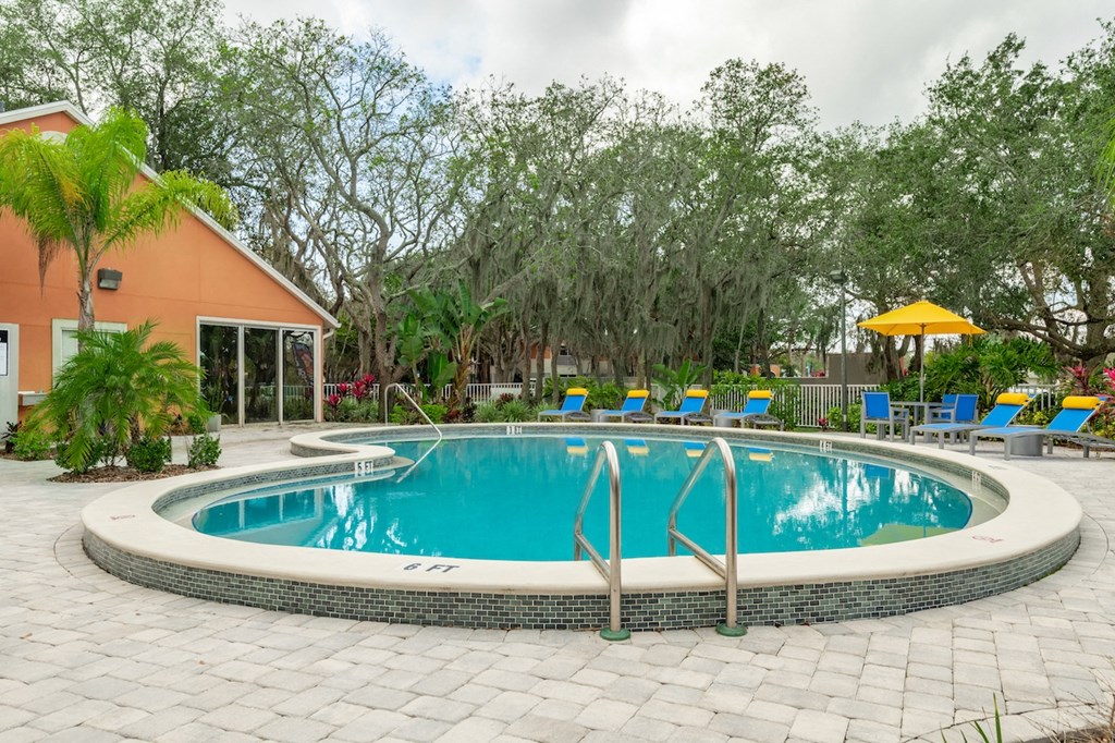 a swimming pool with blue and yellow chaise lounge chairs and trees in the background