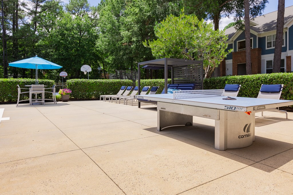 a ping pong table in a courtyard with chairs and umbrellas