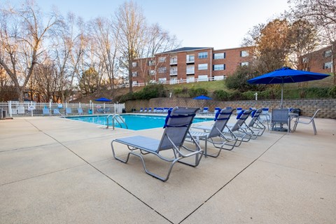 A pool with chairs and umbrellas is surrounded by a brick building at Amelia Village apartments in Clayton, NC.