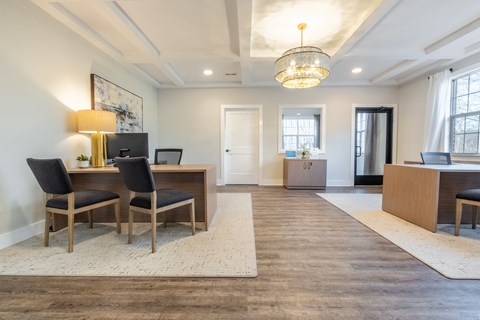 A room with a desk and chairs in the foreground and a doorway in the background in the clubhouse at Amelia Village apartments in Clayton, NC.