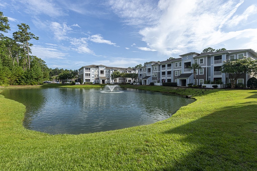 a fountain sits in the middle of a pond in front of an apartment building