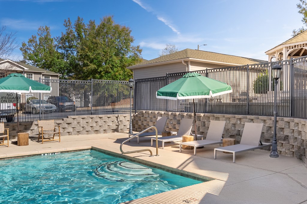 a swimming pool with chairs and umbrellas next to a fence and a house