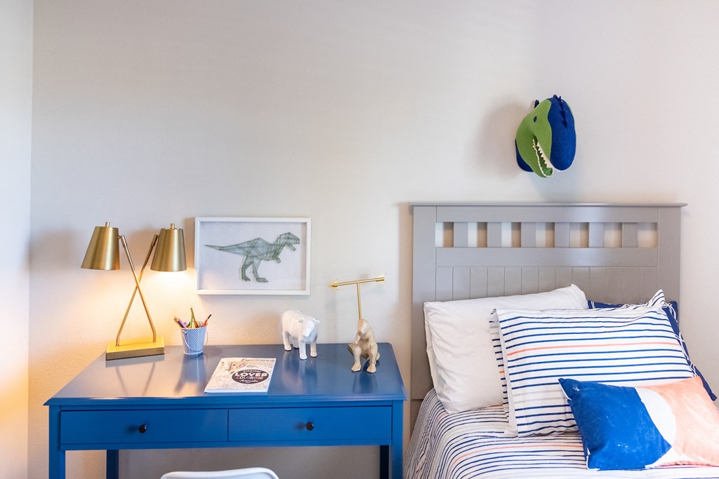 a bedroom with a bed and a blue desk with a desk lamp and a dinosaur