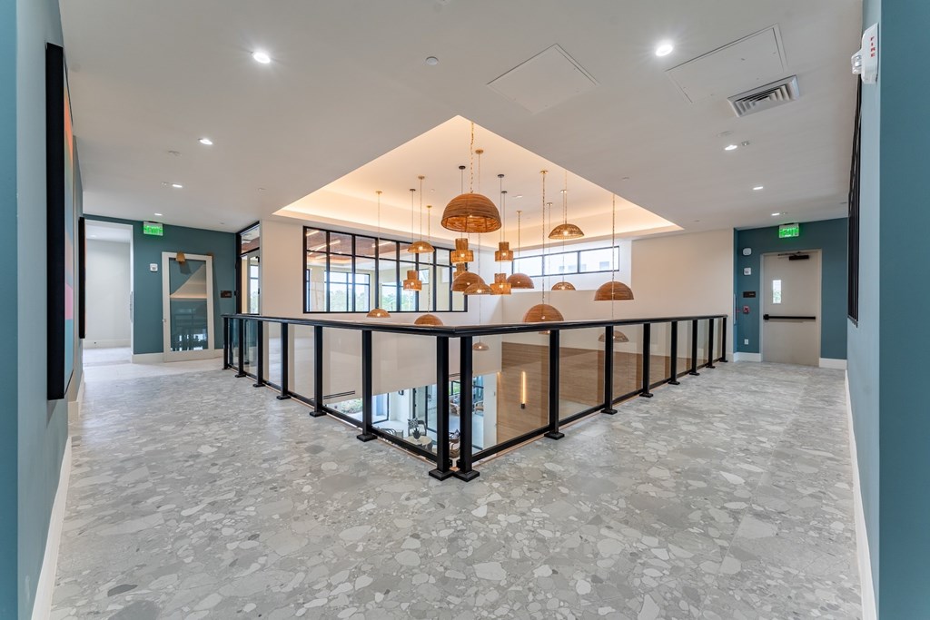 A spacious room with a long table and chairs, and a series of hanging lights.
