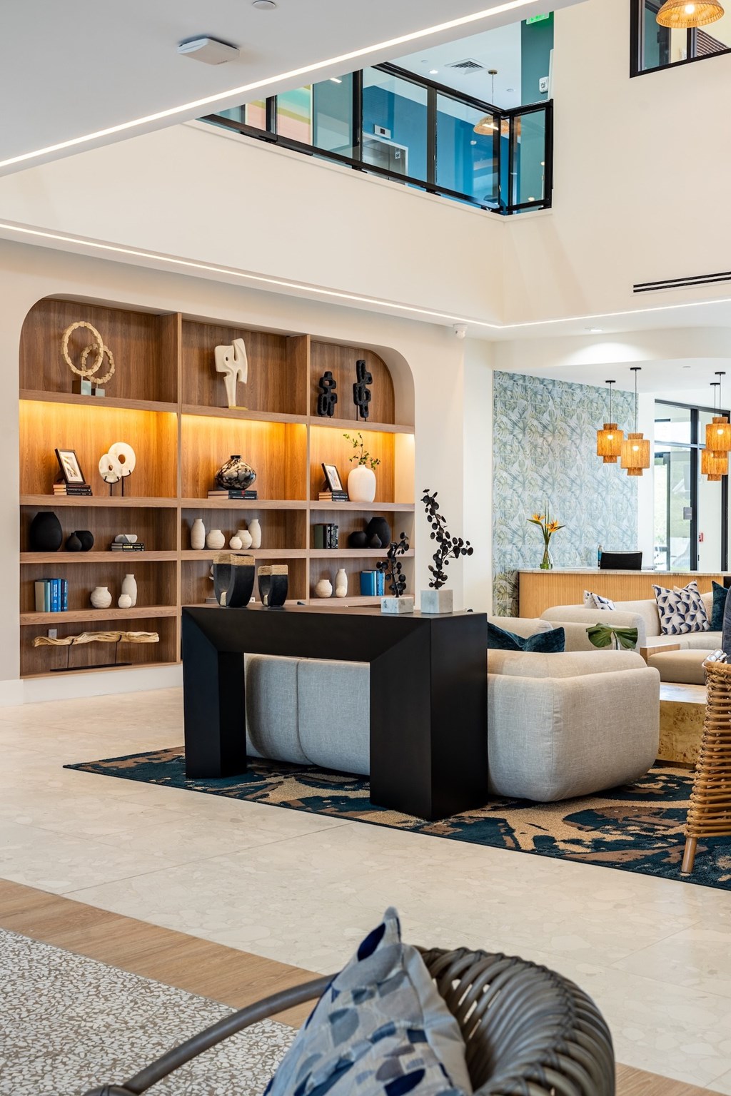 A modern living room with a black and white sofa, a wooden shelf with various decorative items, and a glass wall.