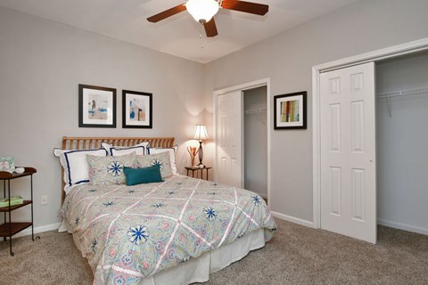 A bedroom with a bed, a ceiling fan, and three pictures on the wall.