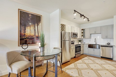 A modern kitchen with a glass table and chairs, a fridge, a microwave, and a painting on the wall.