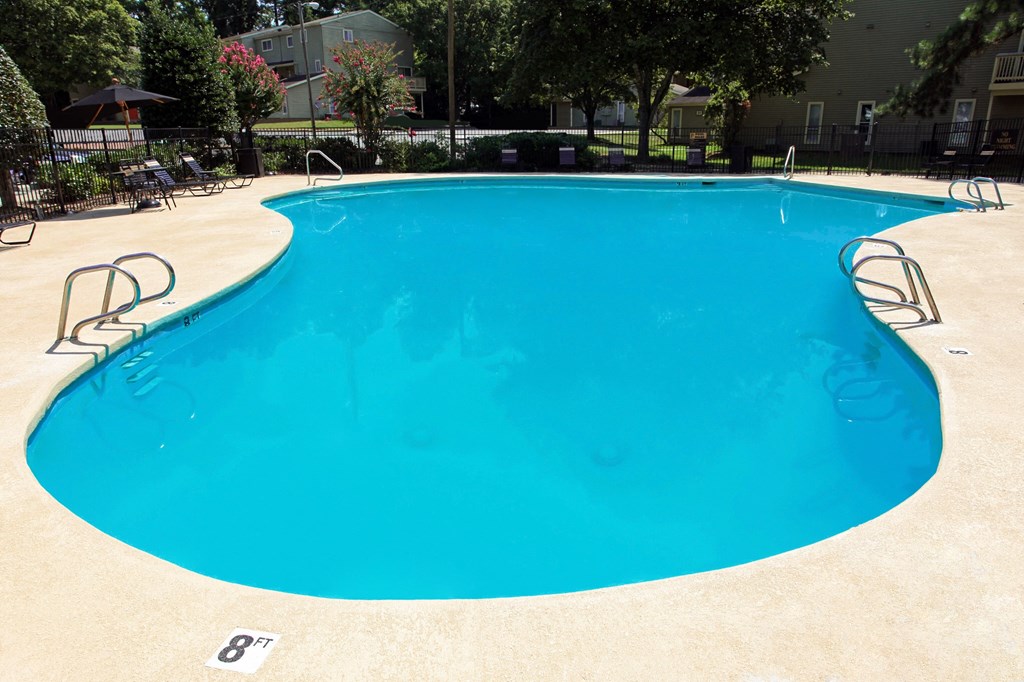 a large blue pool in a yard with chairs and umbrellas
