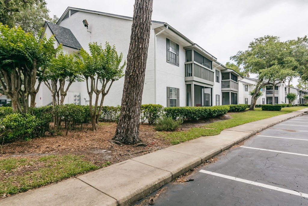 an apartment building with a sidewalk and trees in front of it