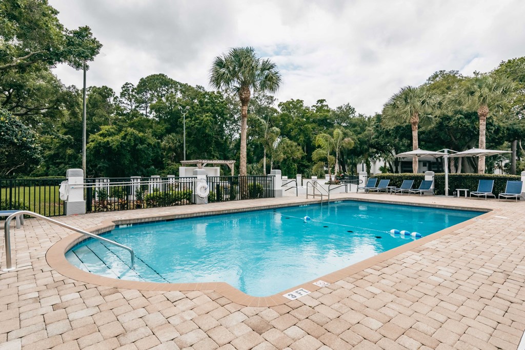 a swimming pool with chairs and trees in the background