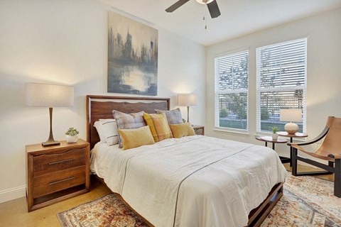 A bedroom with a large bed, a ceiling fan, and a painting on the wall.