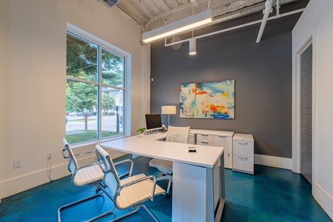 A room with a desk and chairs with a painting on the wall.