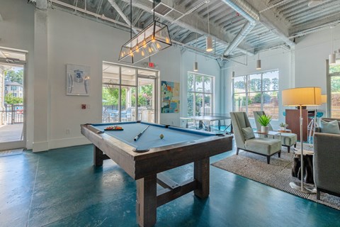 A pool table is in the middle of a room with a chair and a lamp.