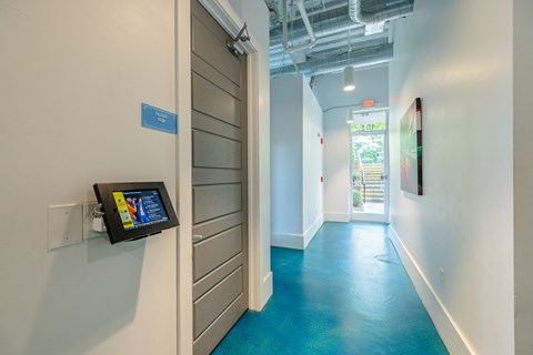 A hallway with a blue floor and a white wall with a tablet on it.