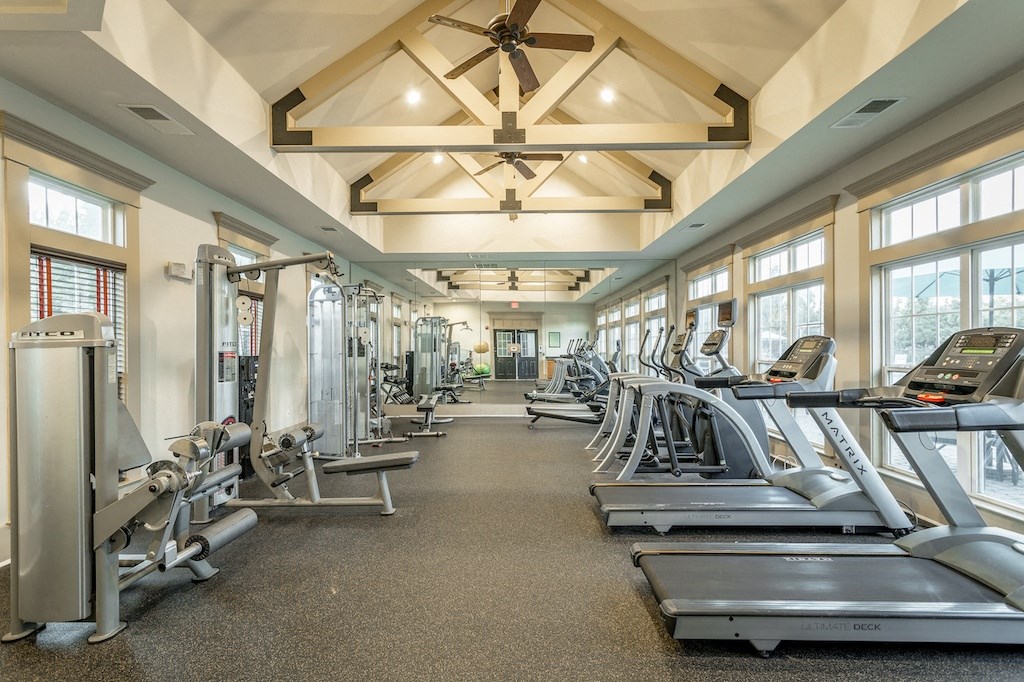 a large fitness room with cardio equipment and windows