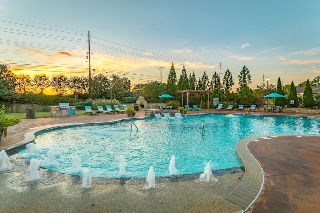 a swimming pool with a fountain and lounge chairs with a sunset in the background