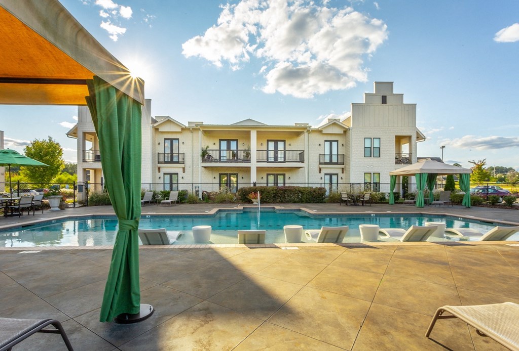a swimming pool with chaise lounge chairs and umbrellas in front of a building