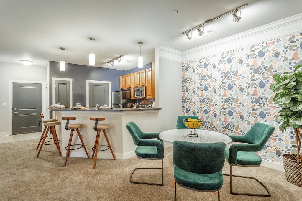 a room with a table and chairs and a kitchen in the background
