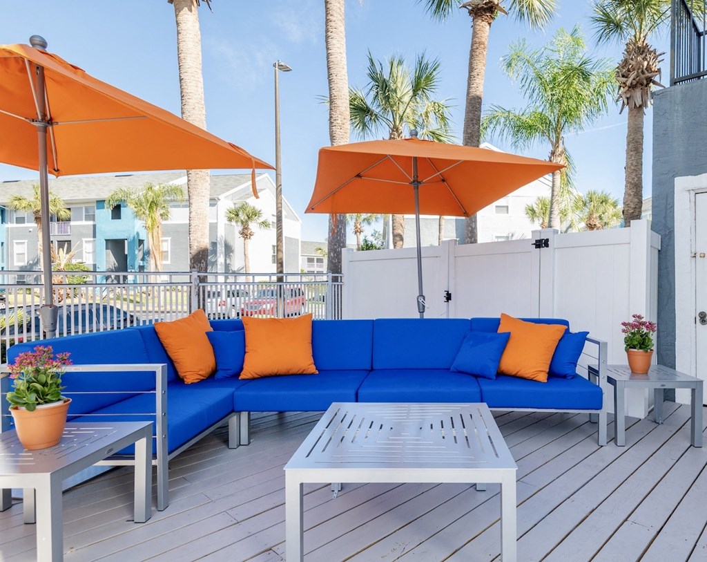 a patio with a blue couch and orange pillows and umbrellas
