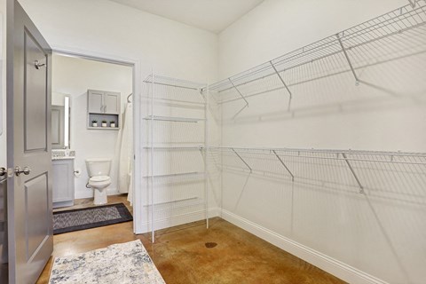A walk in closet with a toilet in the background.