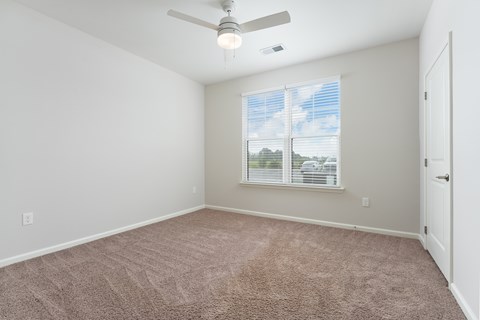 A room with a ceiling fan and carpeted floor at Evolve Holly Ridge Apartments in Holly Ridge, NC.
