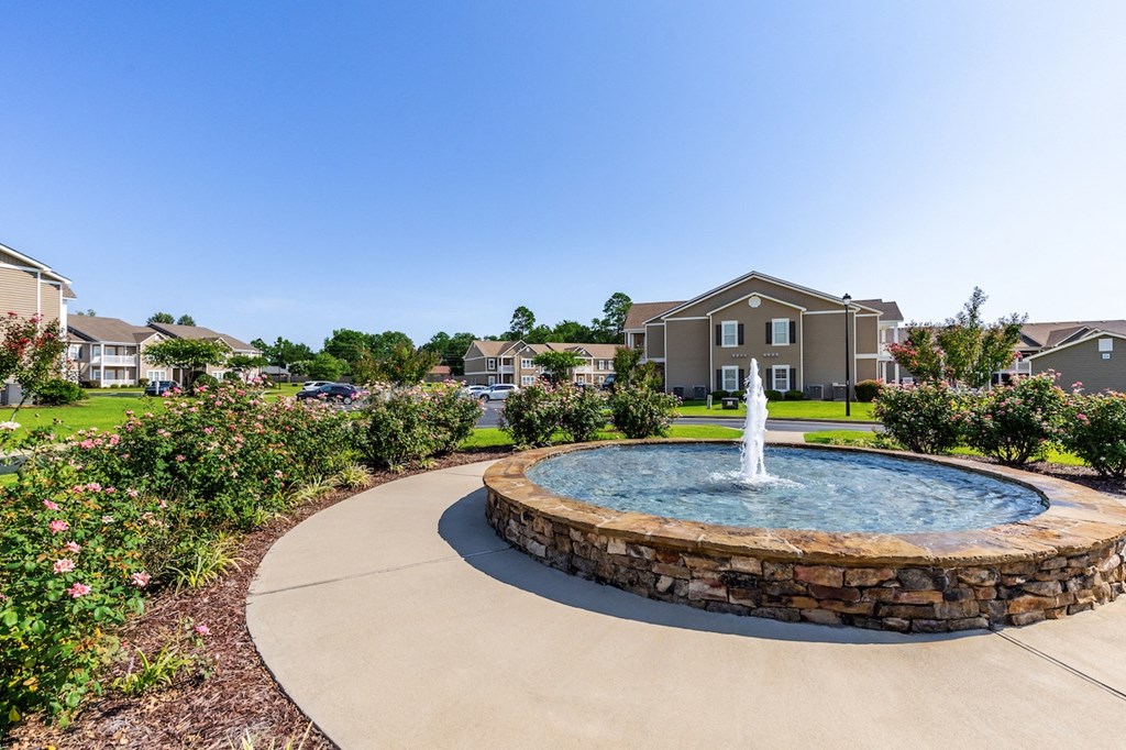a fountain in the center of a garden with houses in the background