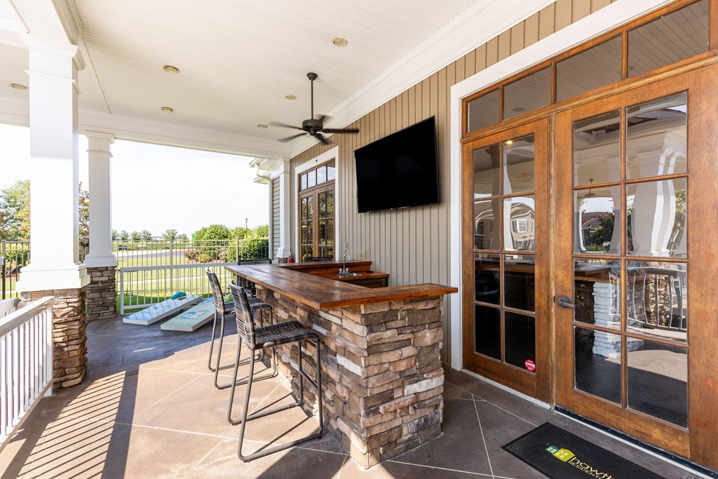 the screened porch has a bar with a stone fireplace and a television