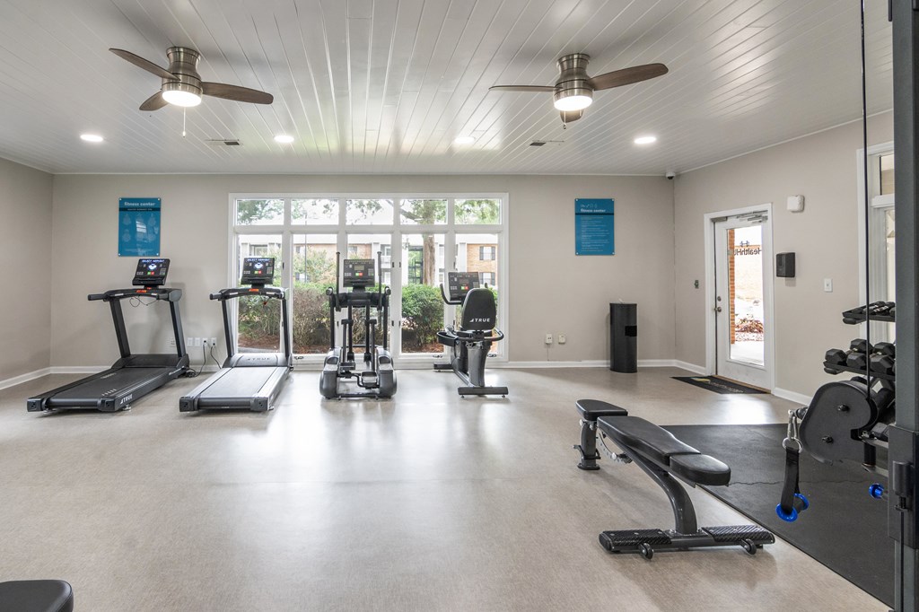 A spacious gym with treadmills, elliptical machines, and a bench press.