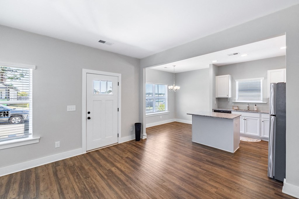 A spacious kitchen and living room with wood flooring and white walls.