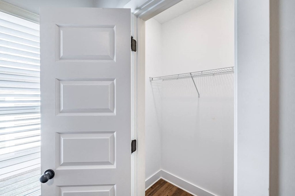 A white door with a black handle is open to a room with a white wall and a wooden floor.