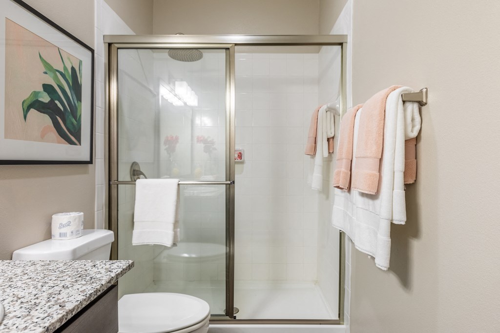 a bathroom with a glass shower and a toilet and towels on a rack