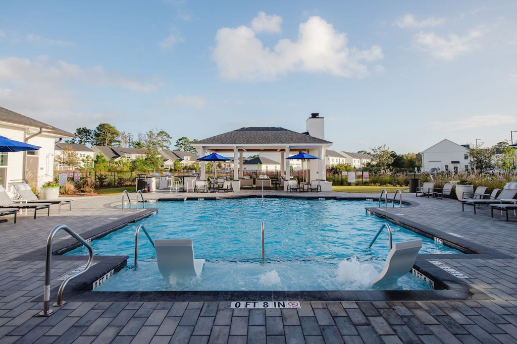 a swimming pool with lounge chairs and umbrellas in front of a resort style clubhouse