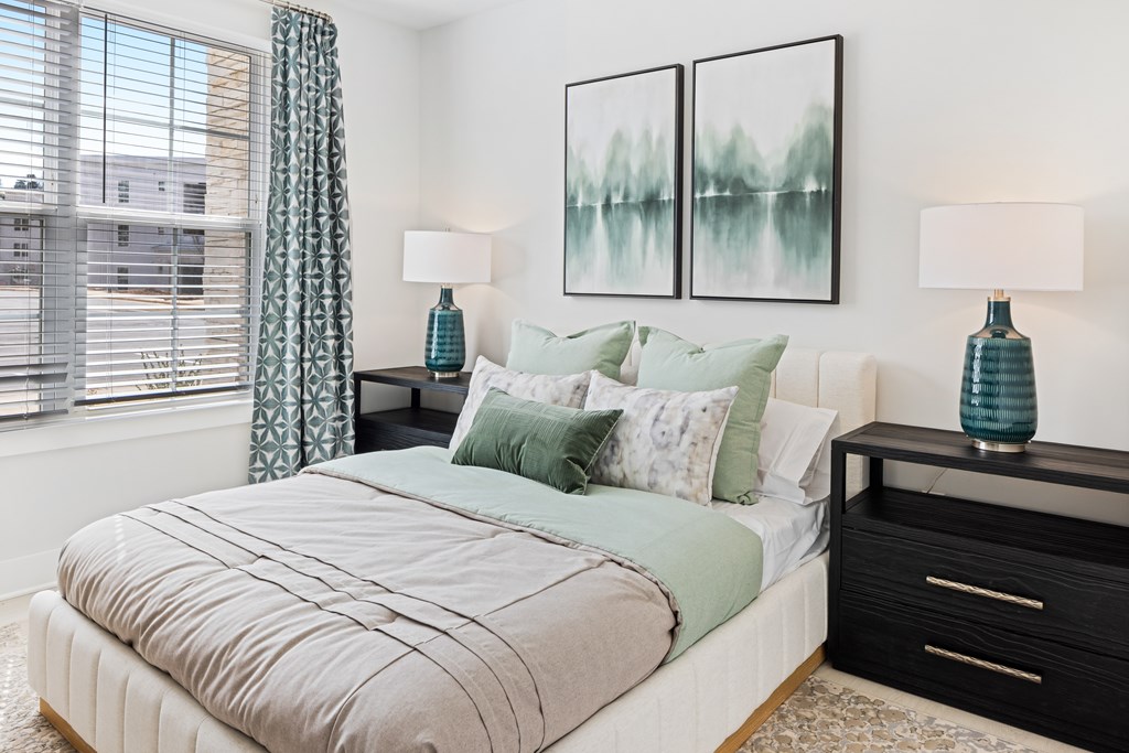 A bedroom with a large bed, two nightstands with lamps, and two framed pictures on the wall at Parker Apartments in Raleigh, NC.