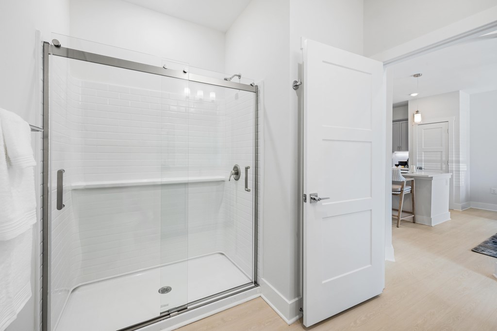 A white bathroom with a glass shower door and a white door at Parker Apartments in Raleigh, NC.