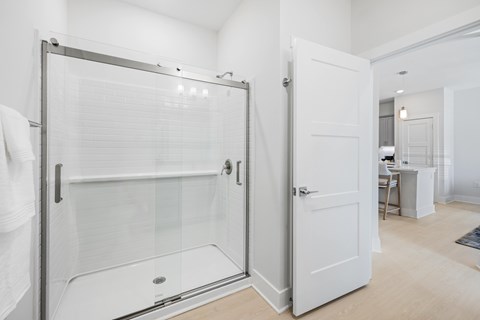 A white bathroom with a glass shower door and a white door at Parker Apartments in Raleigh, NC.