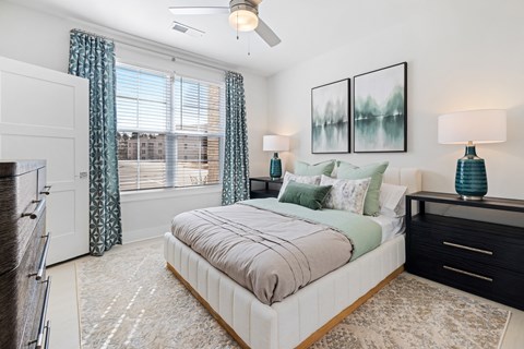 A bedroom with a large bed, a ceiling fan, and a painting on the wall at Parker Apartments in Raleigh, NC.
