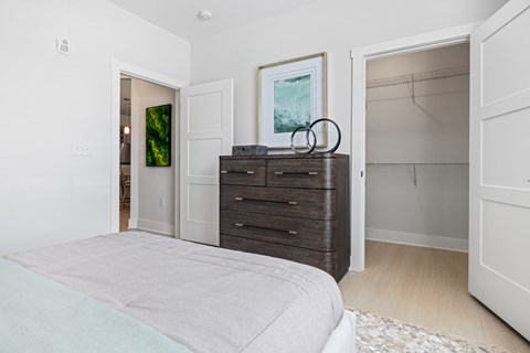 A bedroom with a bed, dresser, and a painting on the wall Parker Apartments in Raleigh, NC.