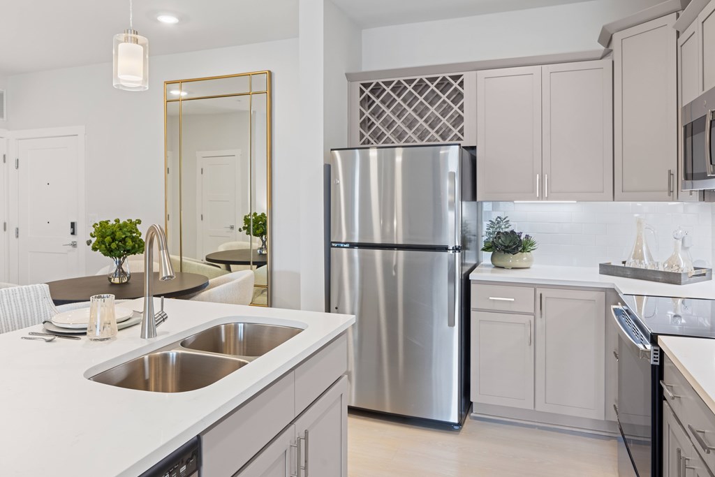 A modern kitchen with a stainless steel refrigerator and a large mirror above the sink at Parker Apartments in Raleigh, NC..